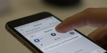 Configurações de Wi-Fi e Bluetooth na tela de um iPhone, com uma mão tocando o dispositivo.